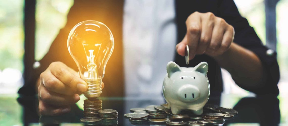 A businesswoman putting coin into piggy bank and a light bulb over coins stack on the table for saving money and financial concept