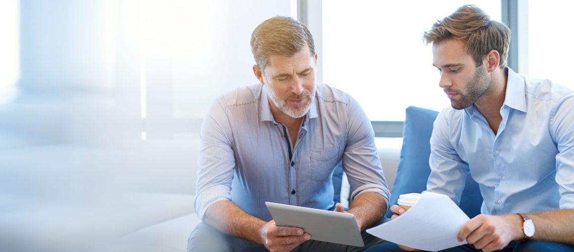 Mature businessman using a digital tablet to discuss information with a younger colleague in a modern business lounge